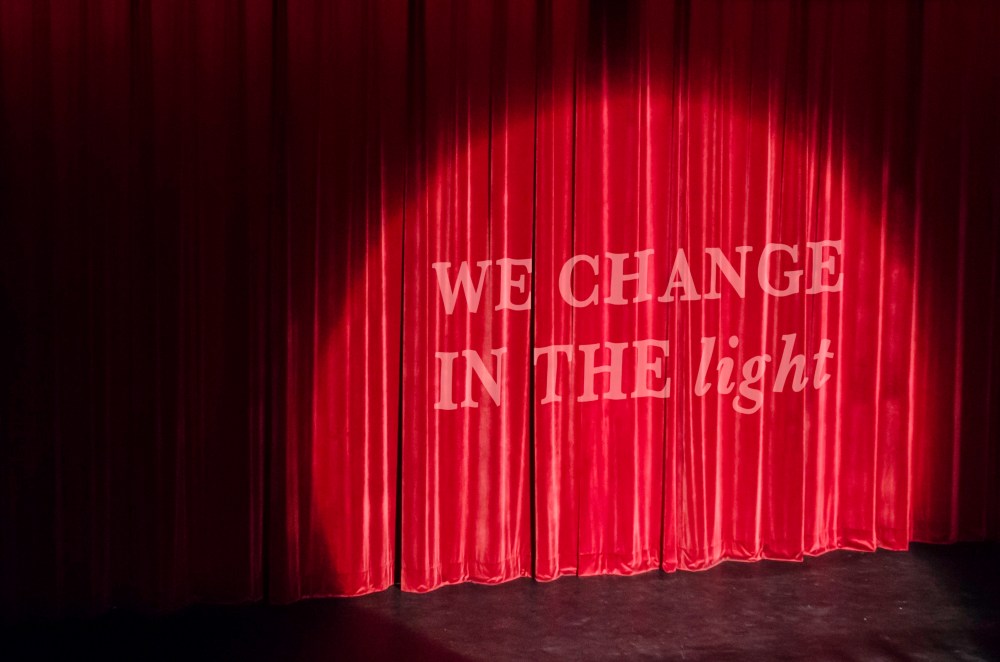 Theatre Curtain - with the words "we change in the light" overlaid upon it.