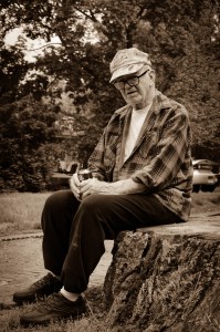 An older gentleman relaxes on an old stump.
