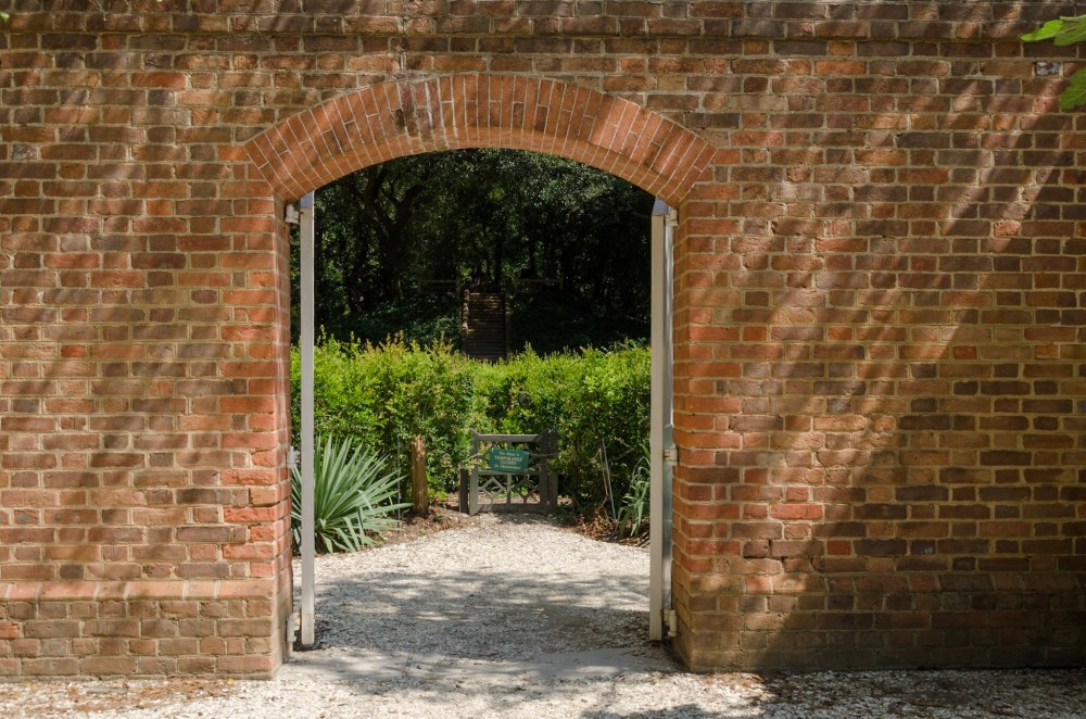 Open Gateway in a brick wall, A hedge maze is revealed on the other side.