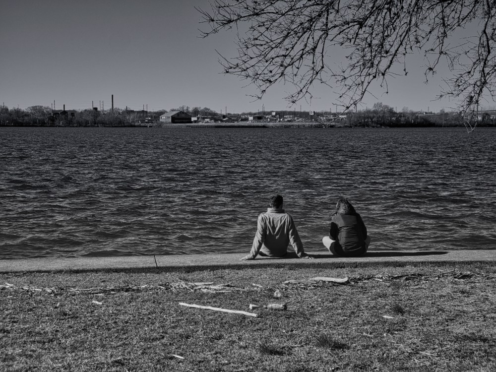 A couple lounges by the river on a mild winter day.