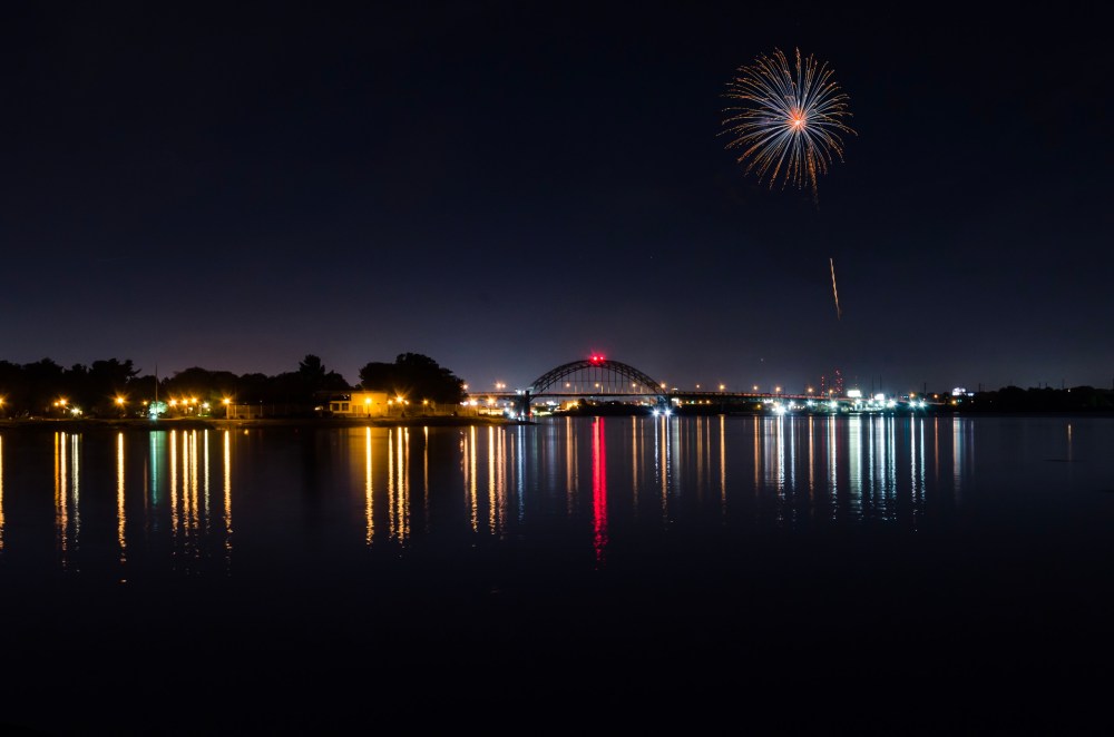 Nighttime photo of the Tacony-Palmyra Bridge. A masked firework photo is in the sky.